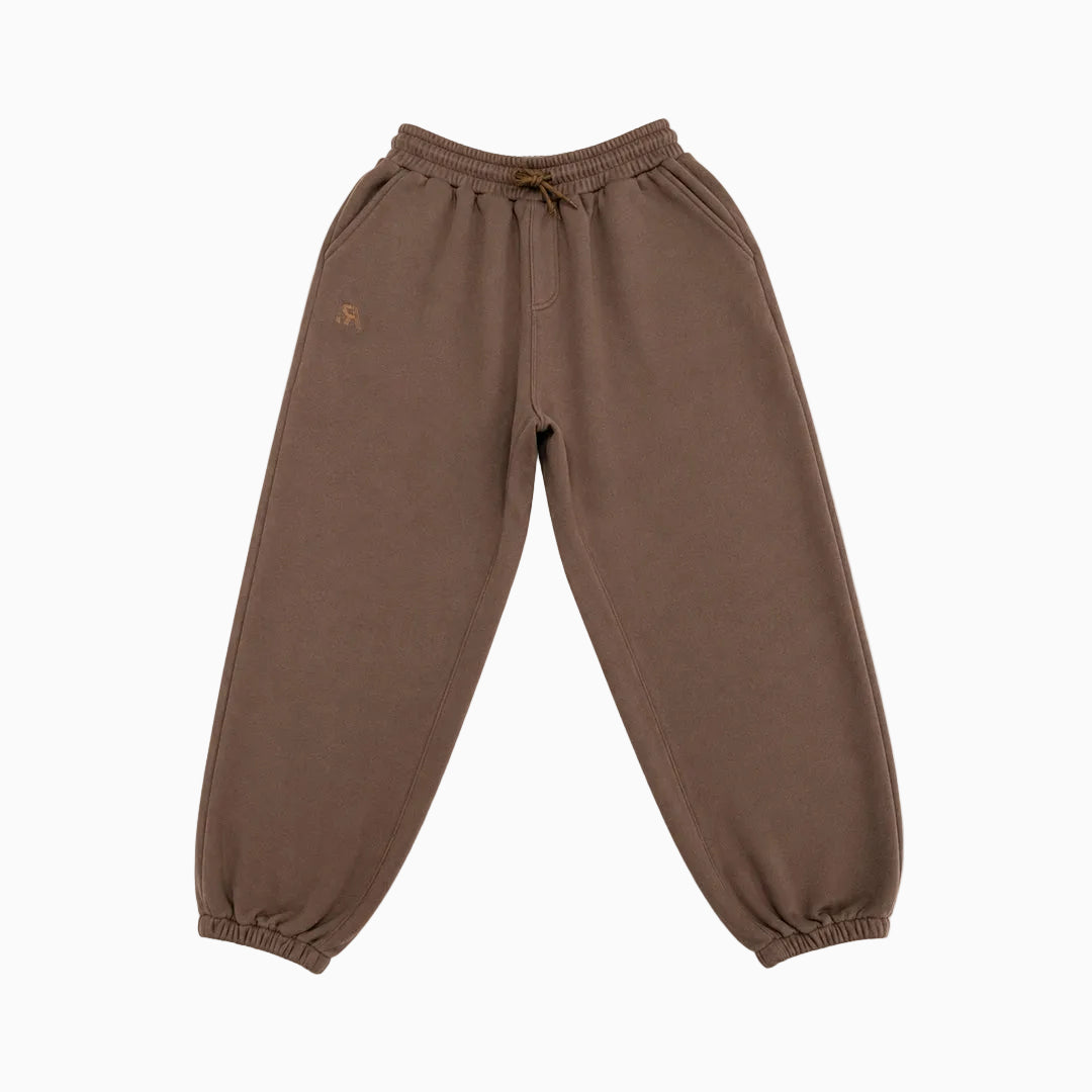 A pair of relaxed-fit jogger sweatpants in a warm brownish-taupe color, featuring an elastic waistband with a matching drawstring and elastic cuffs at the ankles. A small gold embroidered logo is visible on the upper left thigh.