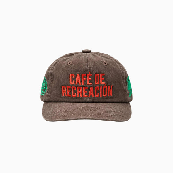 A brown washed cotton baseball cap with 'CAFÉ DE RECREACIÓN' embroidered in red across the front, with green circular patches on the sides, shown against a plain white background.